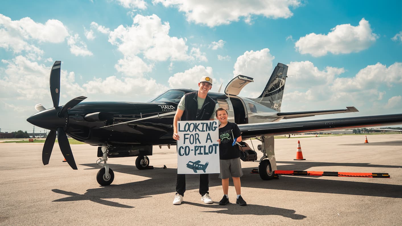 Best Day Ever Foundation recipient holding a 'Looking for a Co-Pilot' sign in front of an airplane